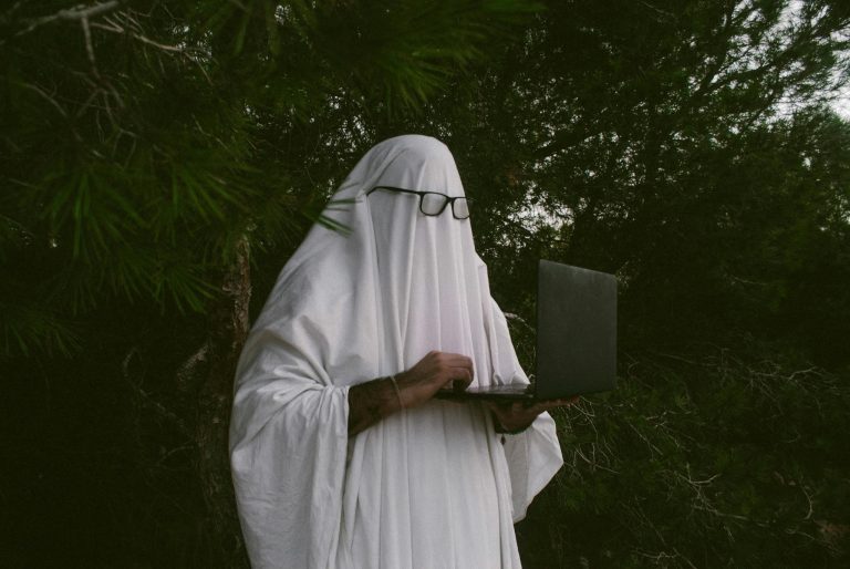 Ghostly figure with glasses using a laptop in a humorous outdoor setting.