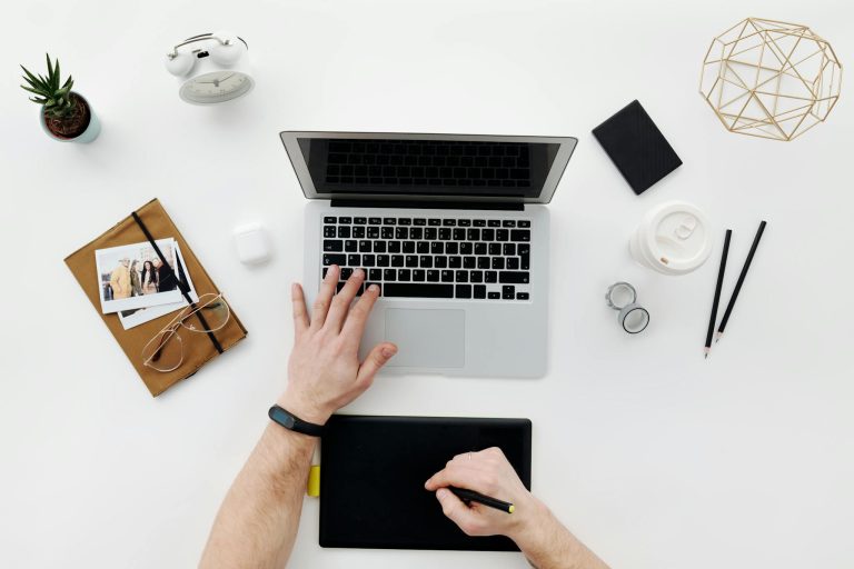 Modern workspace featuring a laptop, drawing tablet, and office essentials from above.