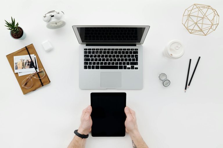 Top view of a clean, modern workspace with a laptop, tablet, and office accessories on a white table.
