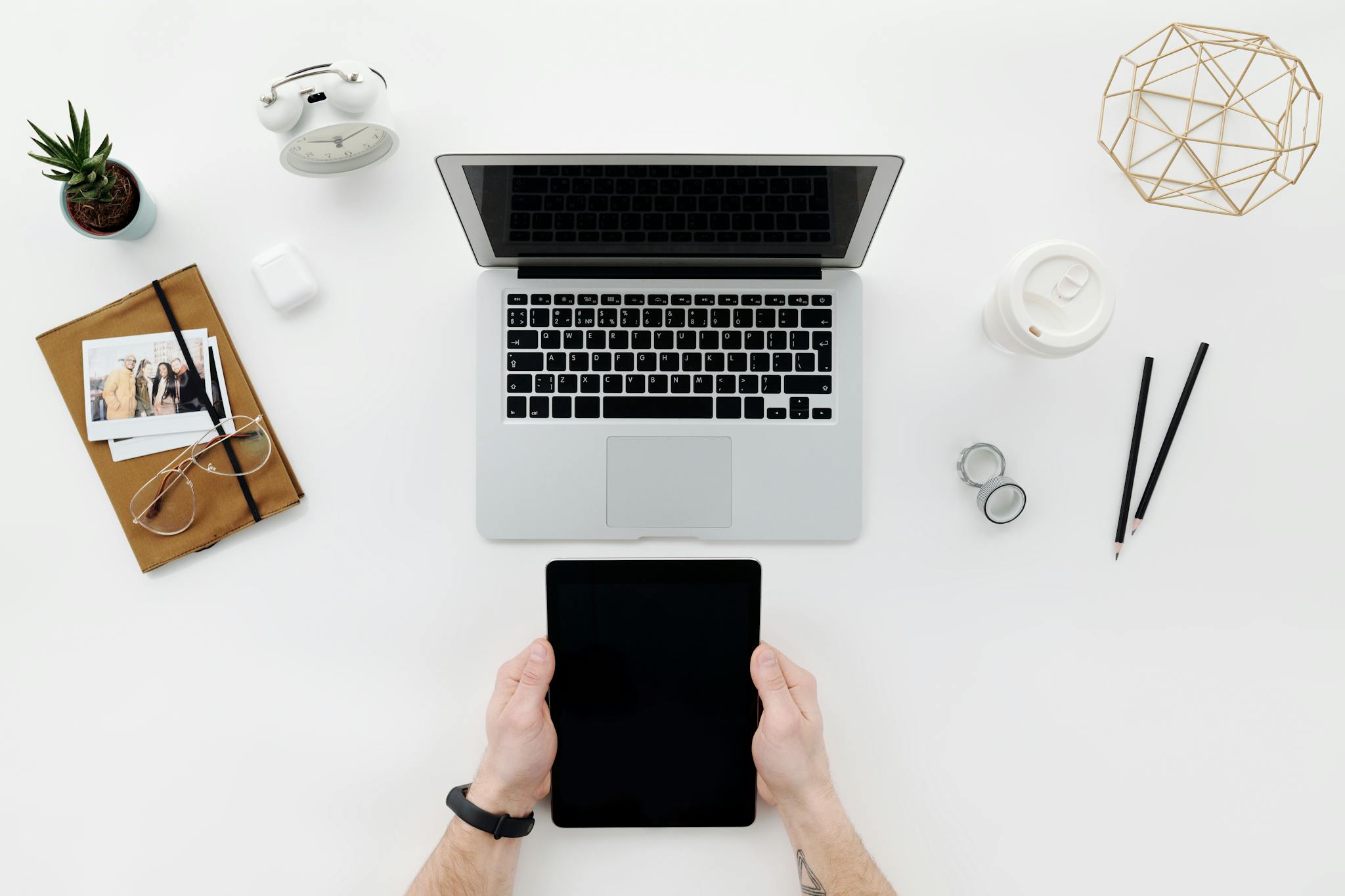 Top view of a clean, modern workspace with a laptop, tablet, and office accessories on a white table.